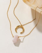 Gold necklaces, one with a rose quartz point and the other with a crescent pendant.
