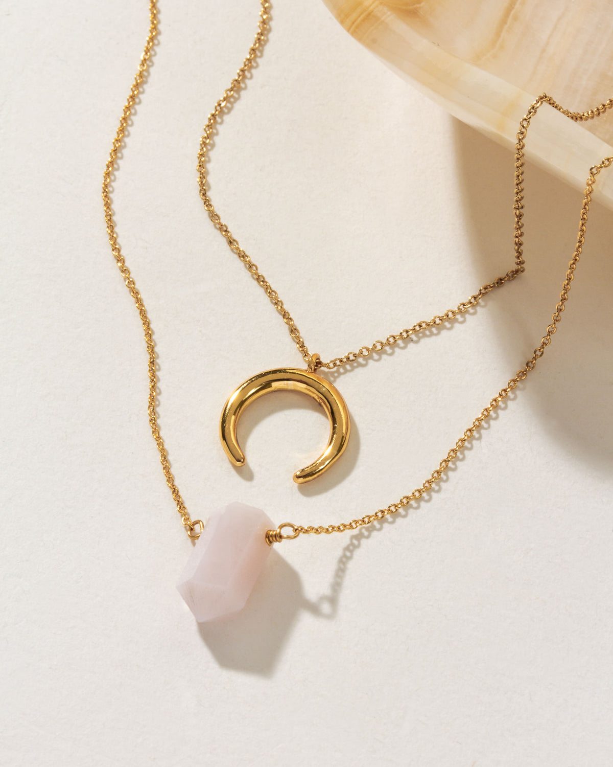 Gold necklaces, one with a rose quartz point and the other with a crescent pendant.