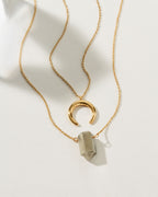 Gold chain necklace set with a crescent pendant and a gray point pendant.