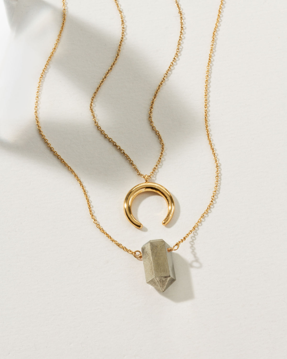 Gold chain necklace set with a crescent pendant and a gray point pendant.