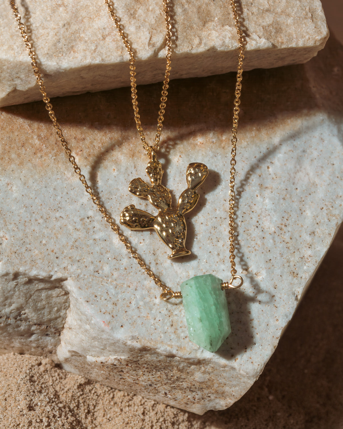 Gold necklace with a cactus pendant and green stone on a textured stone surface