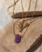 Gold necklace with a purple crystal pendant on a stone surface