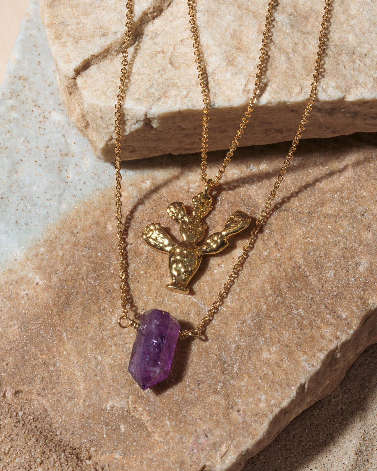 Gold necklace with a purple crystal pendant on a stone surface