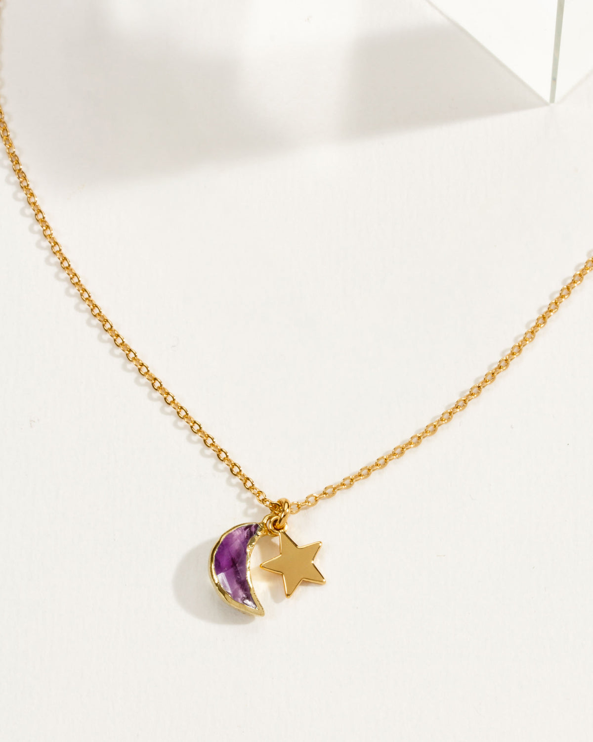 A delicate gold chain necklace featuring a amethyst crescent moon and star pendant.