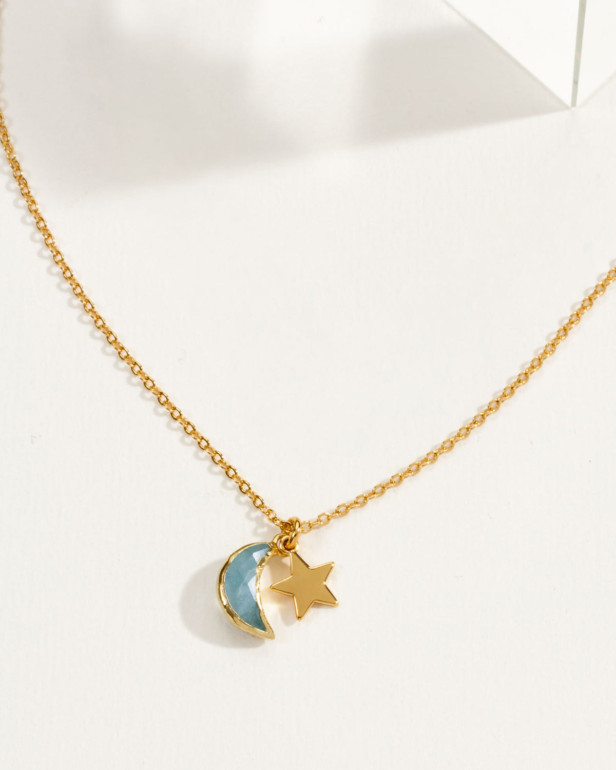 A delicate gold chain necklace featuring a aquamarine crescent moon and star pendant.