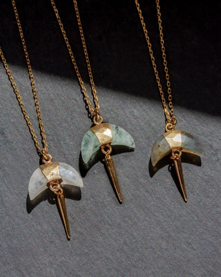 Three gold necklaces with unique crescent horn pendants on a gray surface