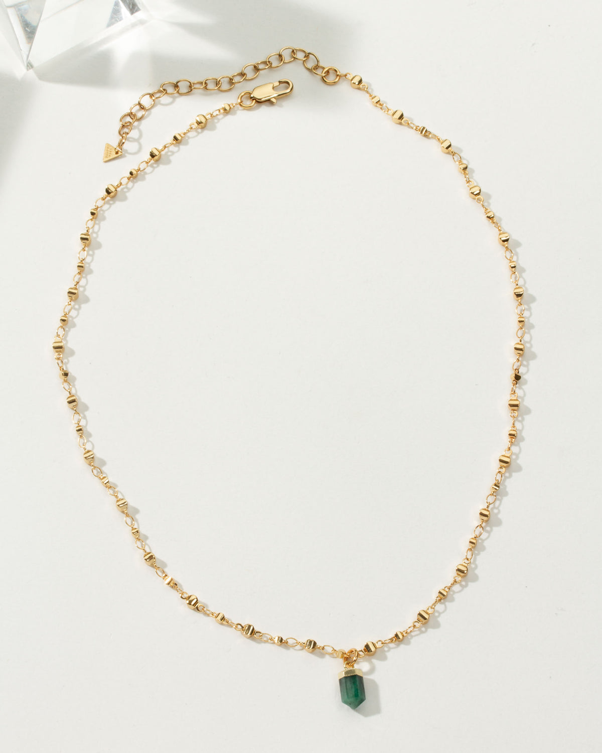 Gold chain necklace with a green emerald gemstone pendant.