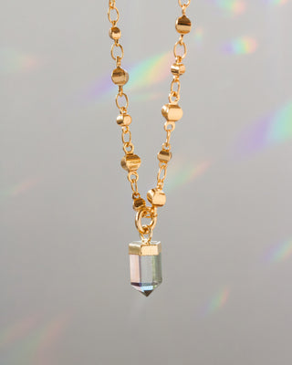 Gold necklace with a crystal pendant on a gray background