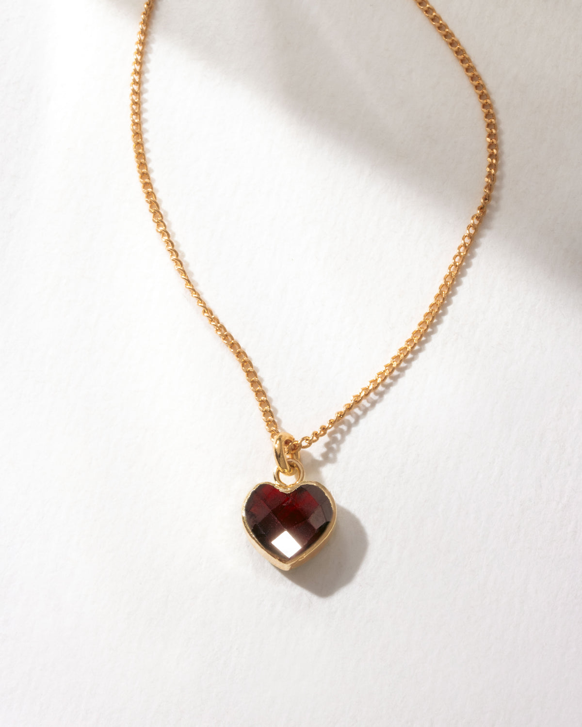 Gold dainty necklace with faceted garnet heart charm.