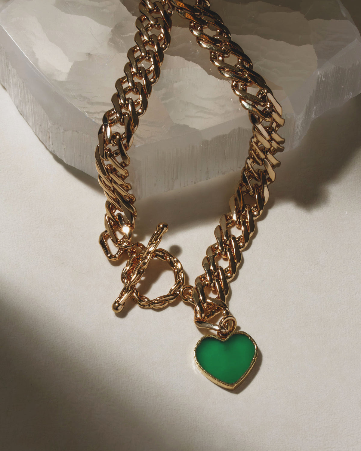 Gold chain necklace with toggle clasp and a green gemstone heart pendant.