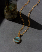 Gold necklace with a blue pendant on a dark surface