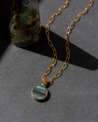 Gold necklace with a blue pendant on a dark surface
