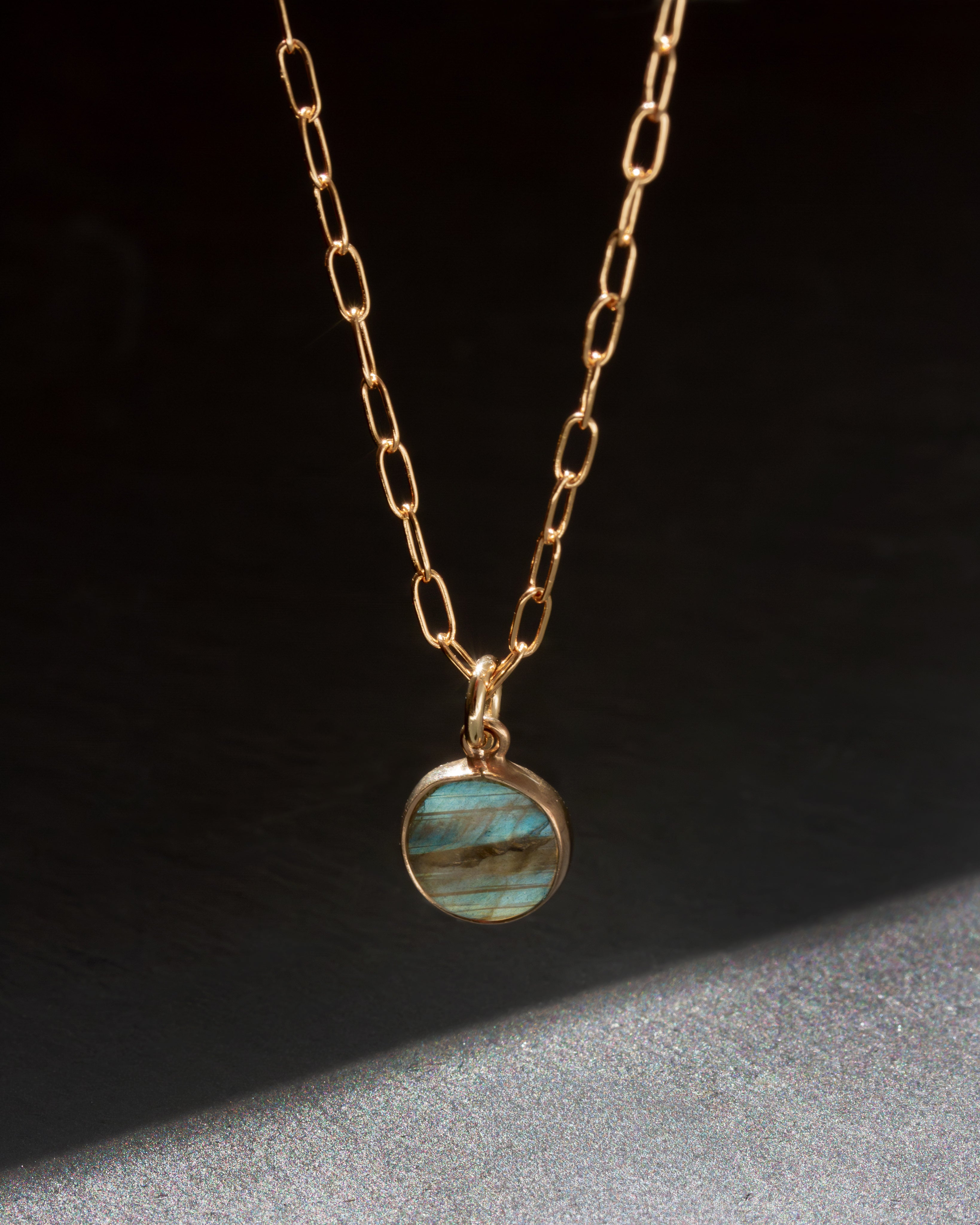 Gold necklace with alabradorite pendant on a dark background