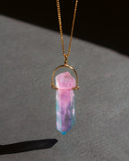 Necklace with a pink and blue crystal pendant on a dark surface