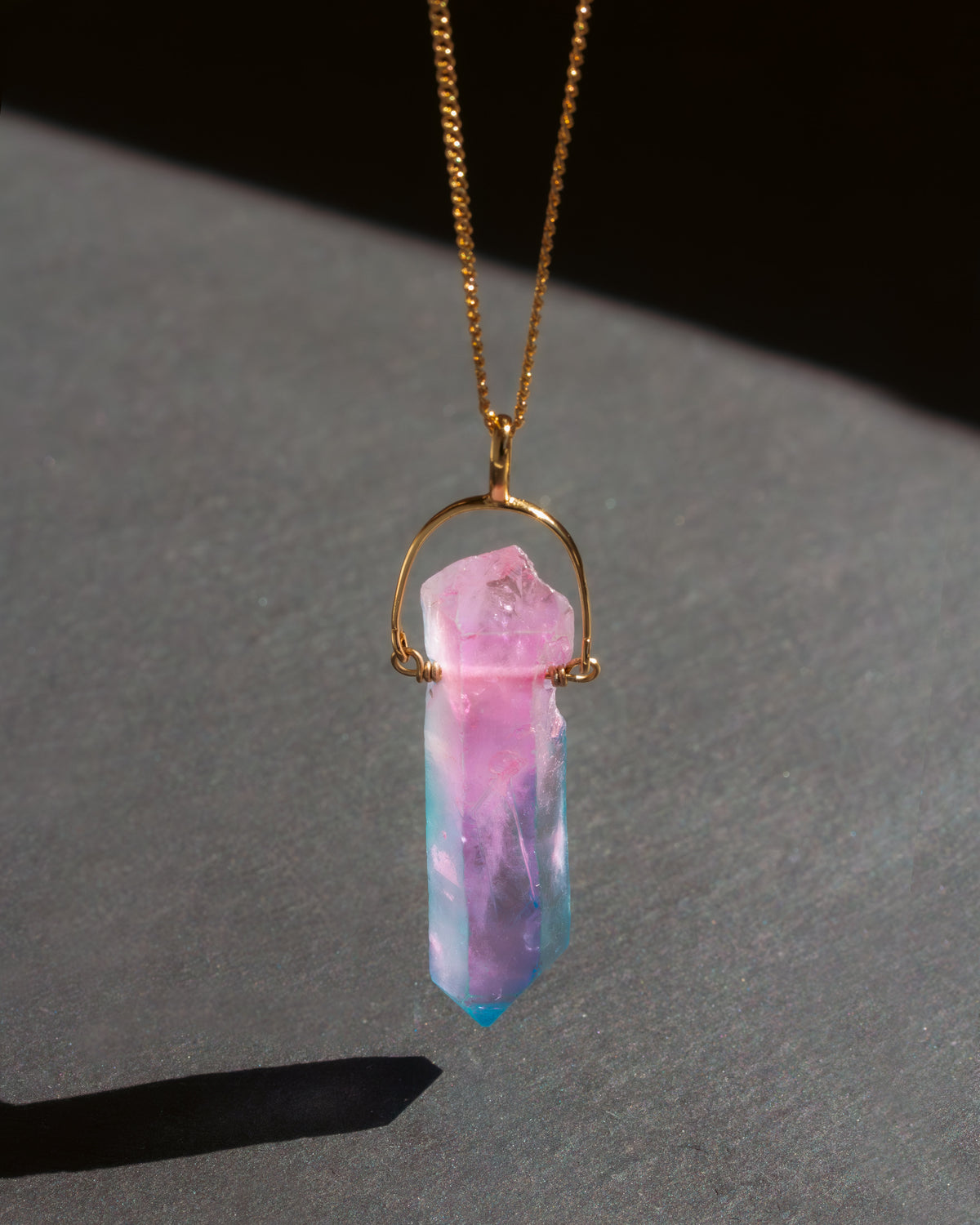 Necklace with a pink and blue crystal pendant on a dark surface