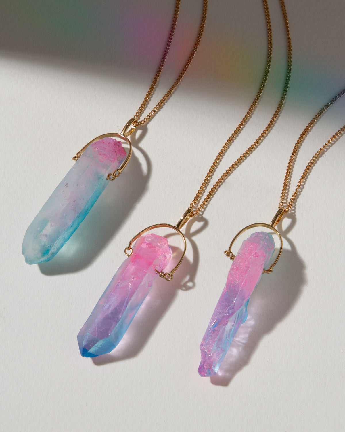 Three crystal pendant necklaces on gold chains against a white background