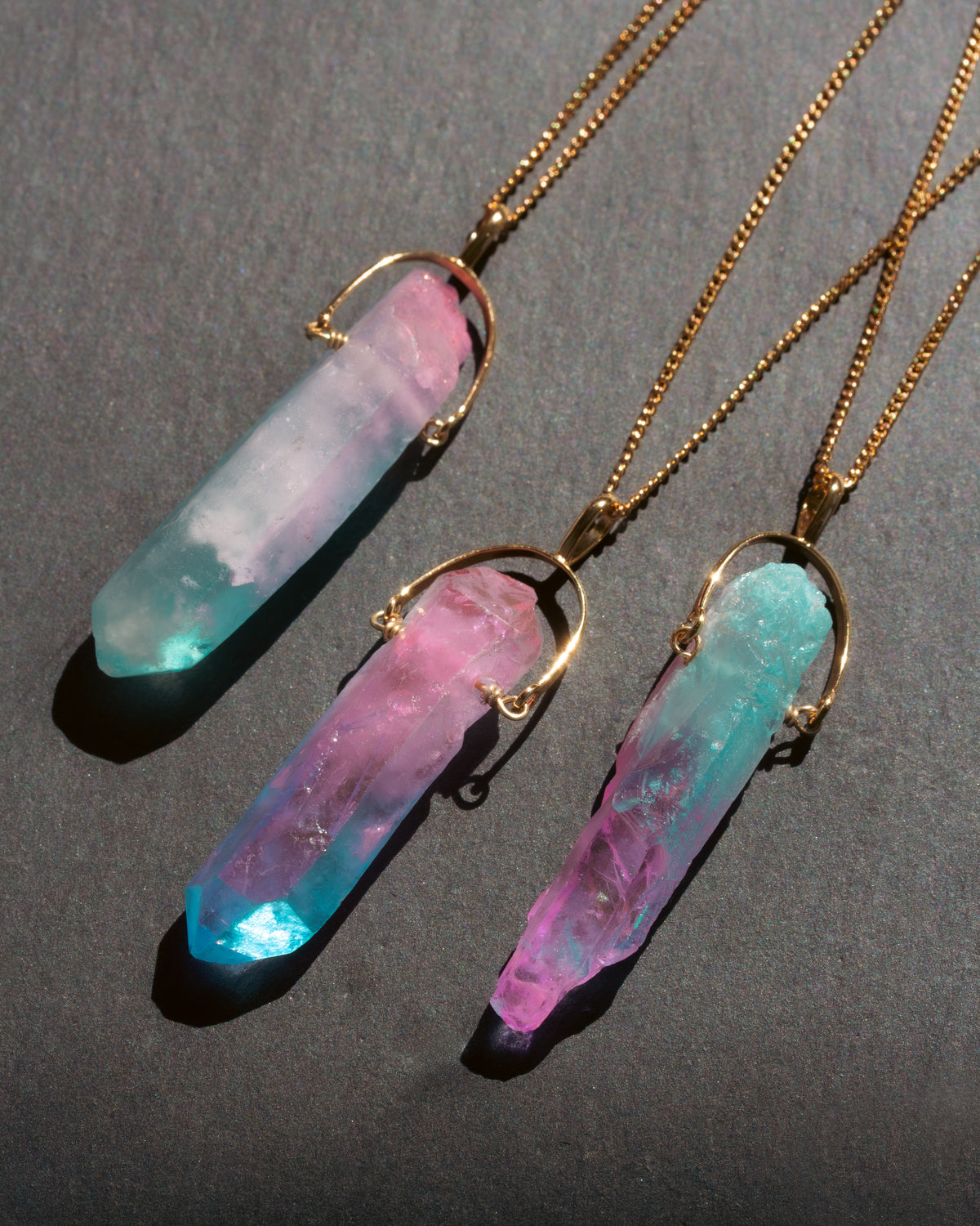 Three crystal necklaces with gold chains on a dark gray background
