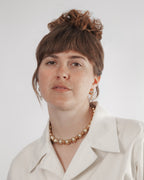 Woman wearing a white shirt and gold necklace against a plain background