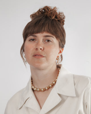Woman wearing a white shirt and gold necklace against a plain background
