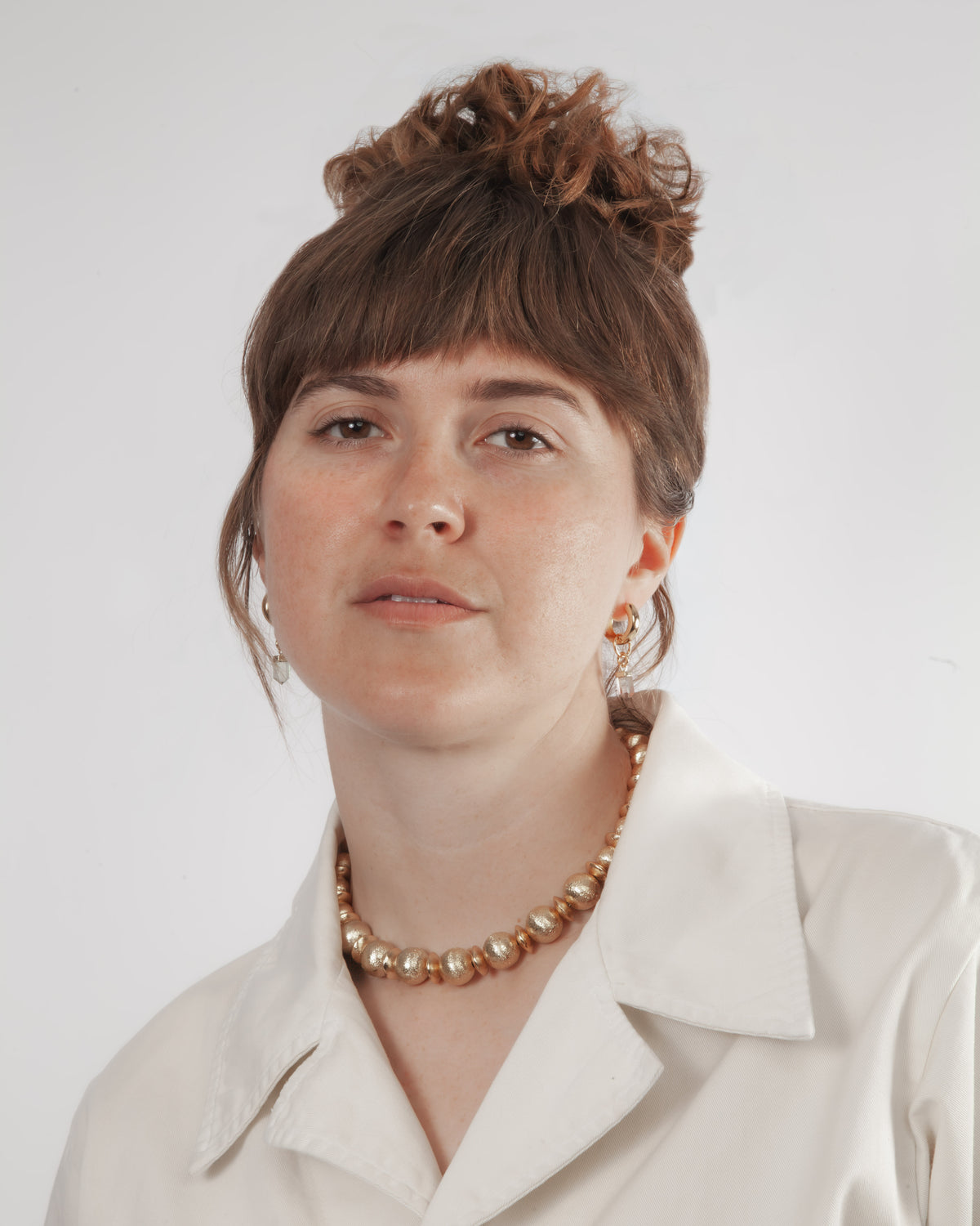 Woman wearing a white shirt and gold necklace against a plain background