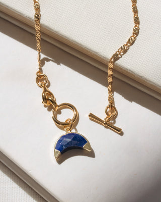 Gold necklace with a blue pendant on a white surface