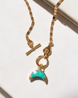 Gold necklace with a turquoise charm on a light background