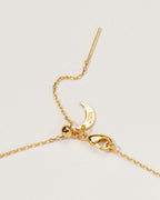 Gold necklace clasp detail moon logo charm on a light gray background