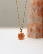 Gold necklace with a orange pendant on a neutral background