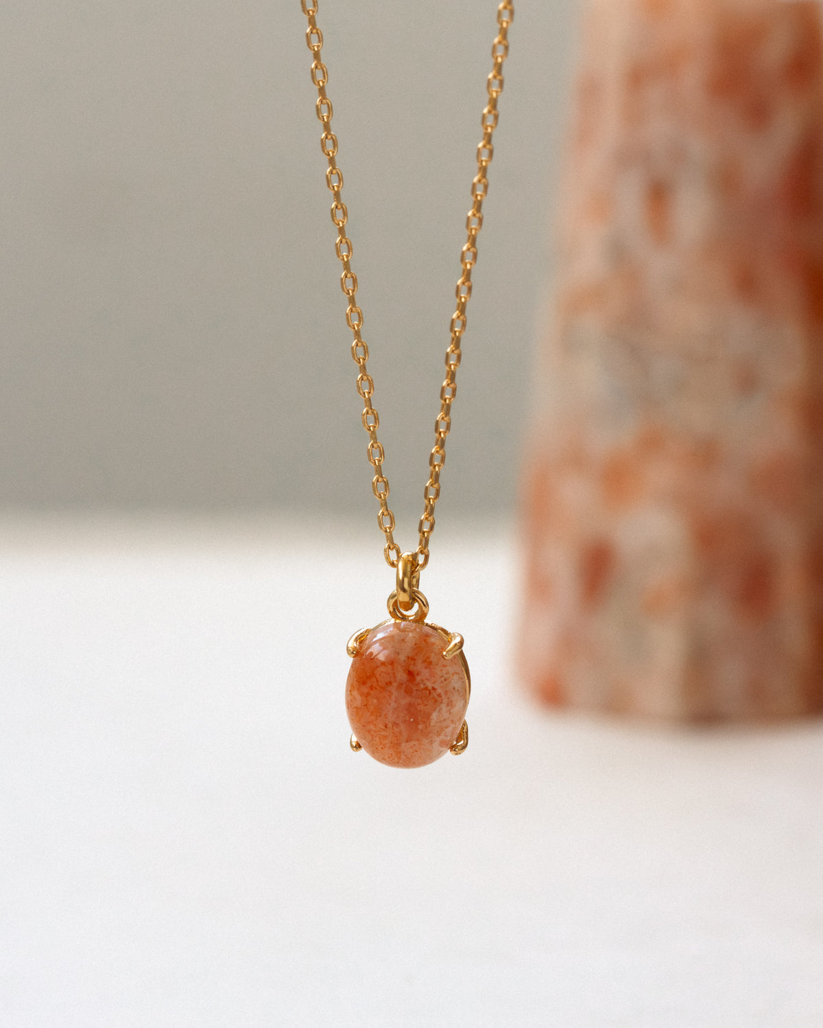 Gold necklace with a orange pendant on a neutral background