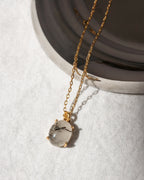Gold necklace with a clear pendant on a light gray background