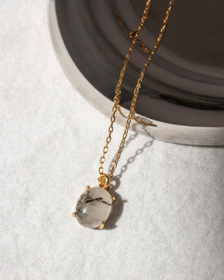 Gold necklace with a clear pendant on a light gray background