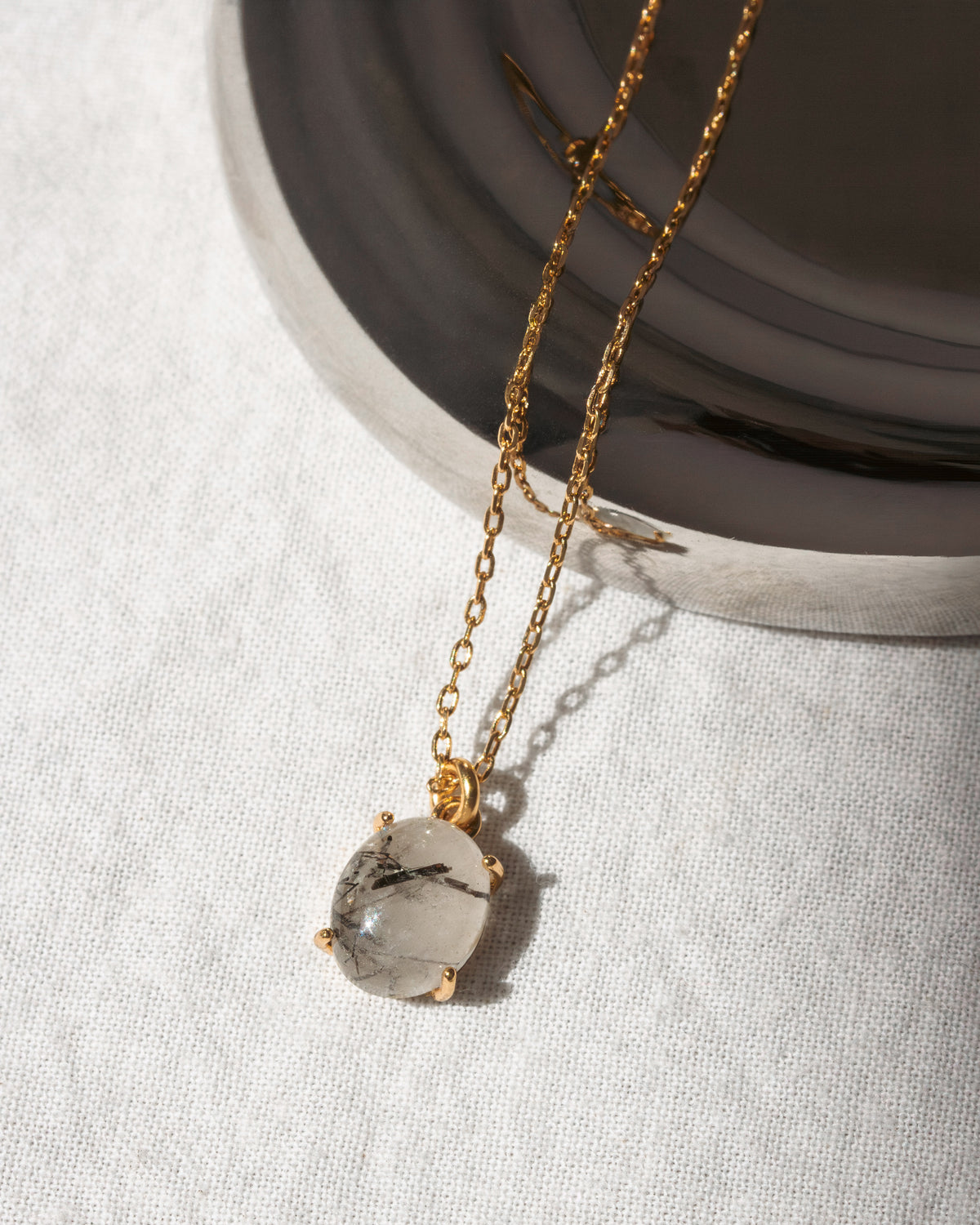 Gold necklace with a clear pendant on a light gray background