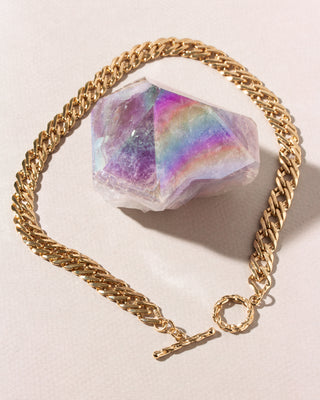 A gold-toned curb chain bracelet with a toggle clasp, arranged in a circle around a faceted iridescent crystal.