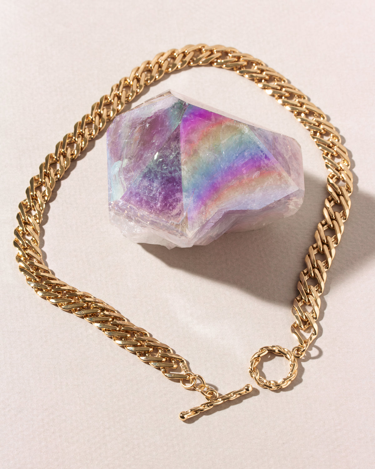 A gold-toned curb chain bracelet with a toggle clasp, arranged in a circle around a faceted iridescent crystal.