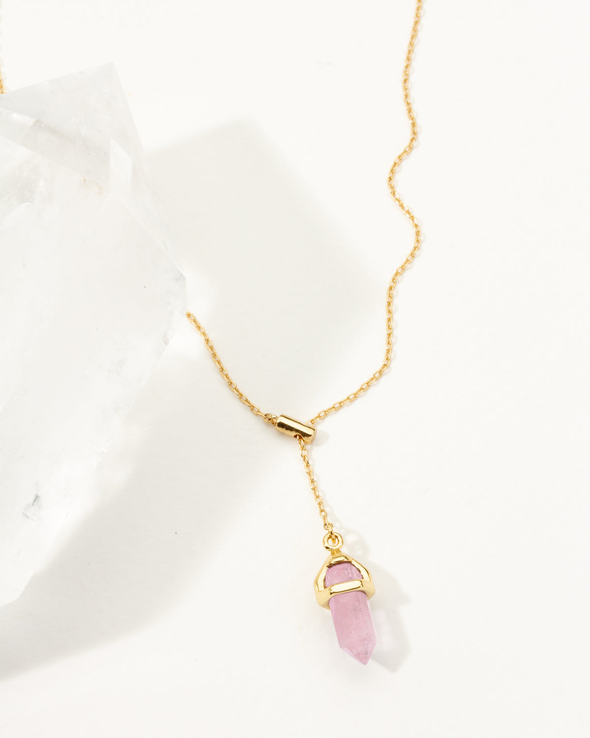 Gold necklace with a pink rose quartz crystal pendant on a white background