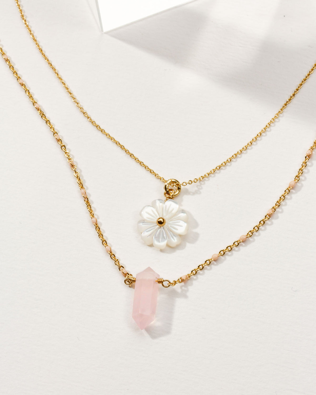 Layered gold necklaces with mother-of-pearl daisy and pink gemstone pendants