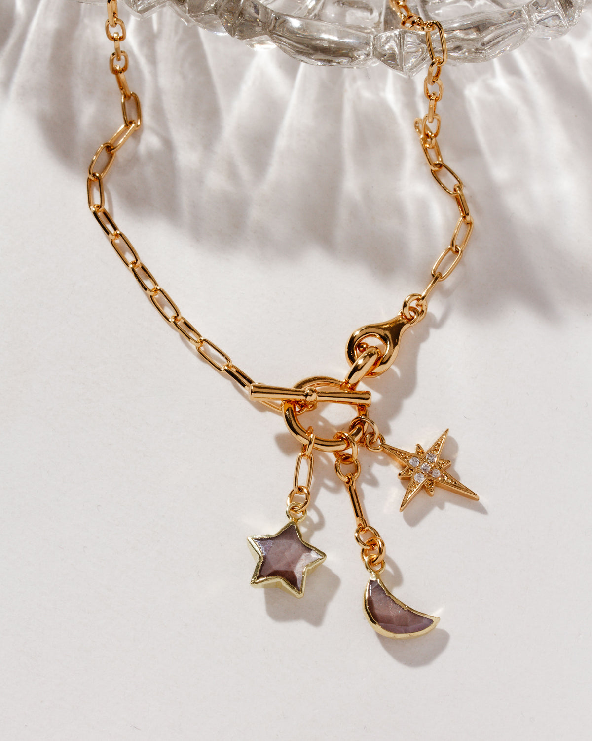 A gold toggle necklace with charms with a crescent moon and stars