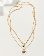 A layered, golden necklace with a heart charm and a coffee moonstone crescent moon charm.