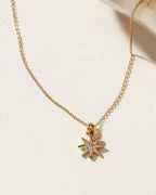 Gold necklace with a starburst pendant and a clear gemstone in the center.