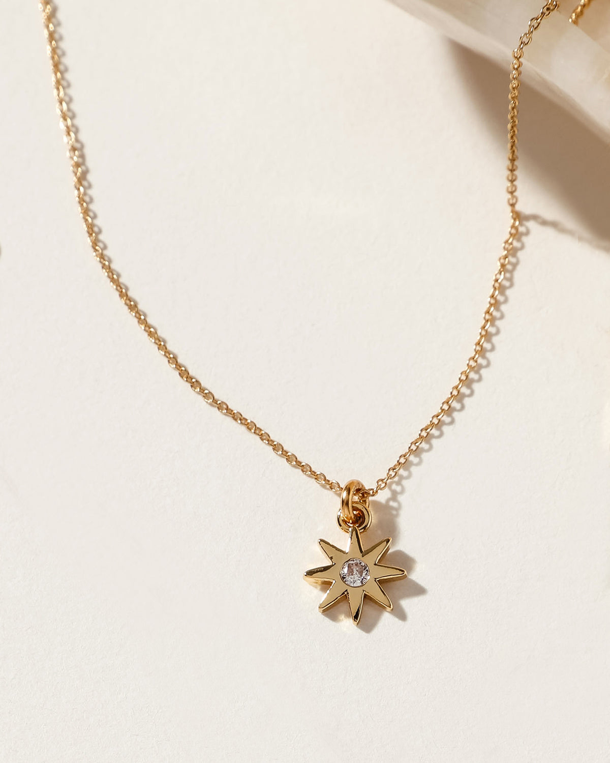 Gold necklace with a starburst pendant and a clear gemstone in the center.