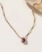 Gold necklace featuring a teardrop shaped, neutral tone gemstone pendant.