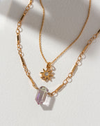 Gold necklaces layered, one with a sun star charm, and one with a mystic quartz stone.