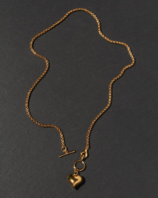 A gold chain necklace with a toggle clasp and a heart-shaped charm.