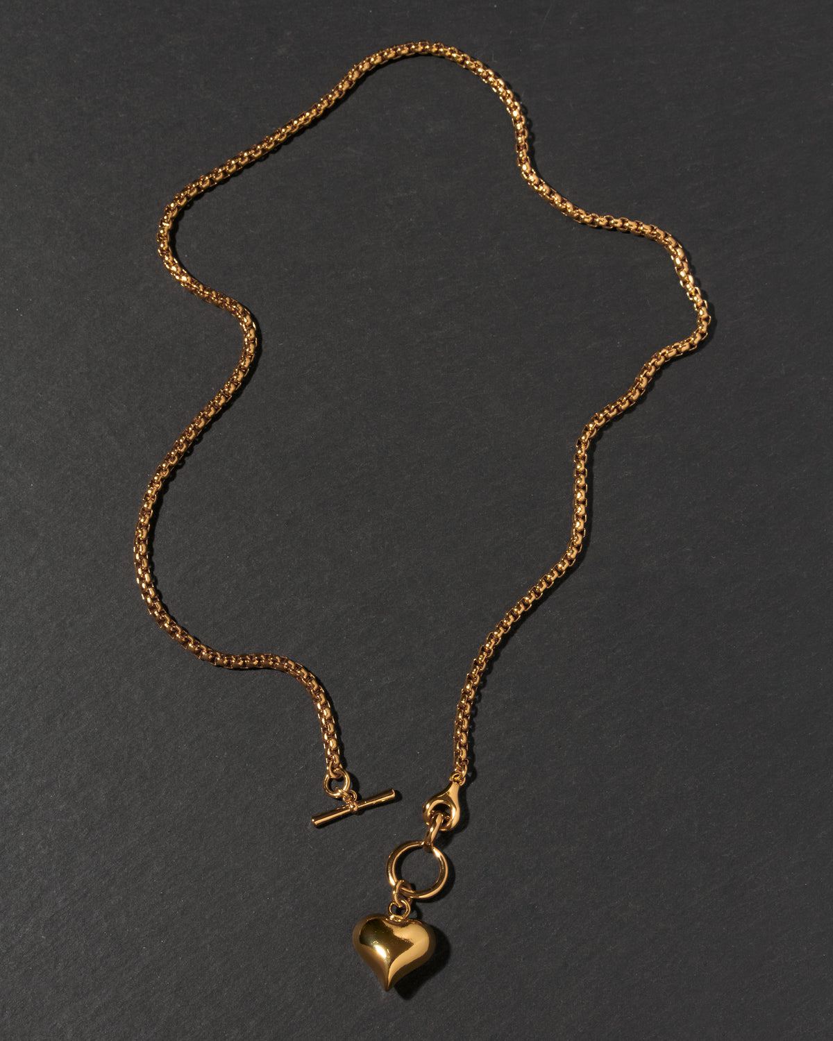 A gold chain necklace with a toggle clasp and a heart-shaped charm.