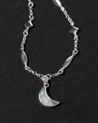A silver-toned necklace featuring a crescent moon moonstone pendant.