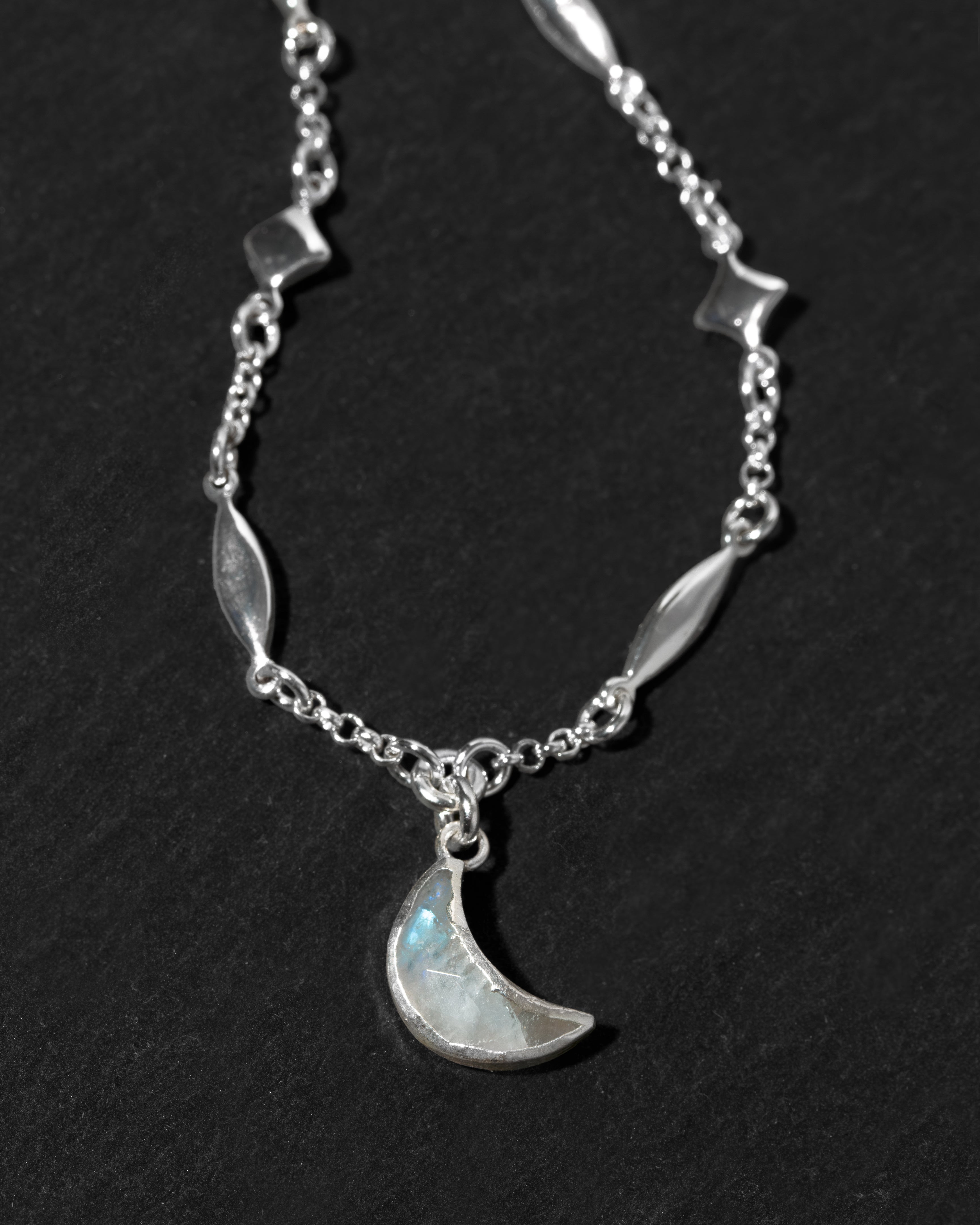 A silver-toned necklace featuring a crescent moon moonstone pendant.