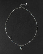 A silver-toned chain necklace featuring small geometric star and diamond-shaped stations, a matching crescent moon pendant, and an adjustable extender chain.