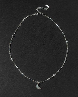 A silver-toned chain necklace featuring small geometric star and diamond-shaped stations, a matching crescent moon pendant, and an adjustable extender chain.