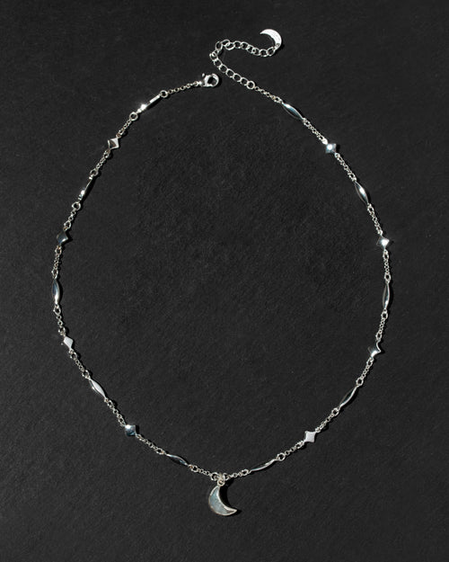 A silver-toned chain necklace featuring small geometric star and diamond-shaped stations, a matching crescent moon pendant, and an adjustable extender chain.