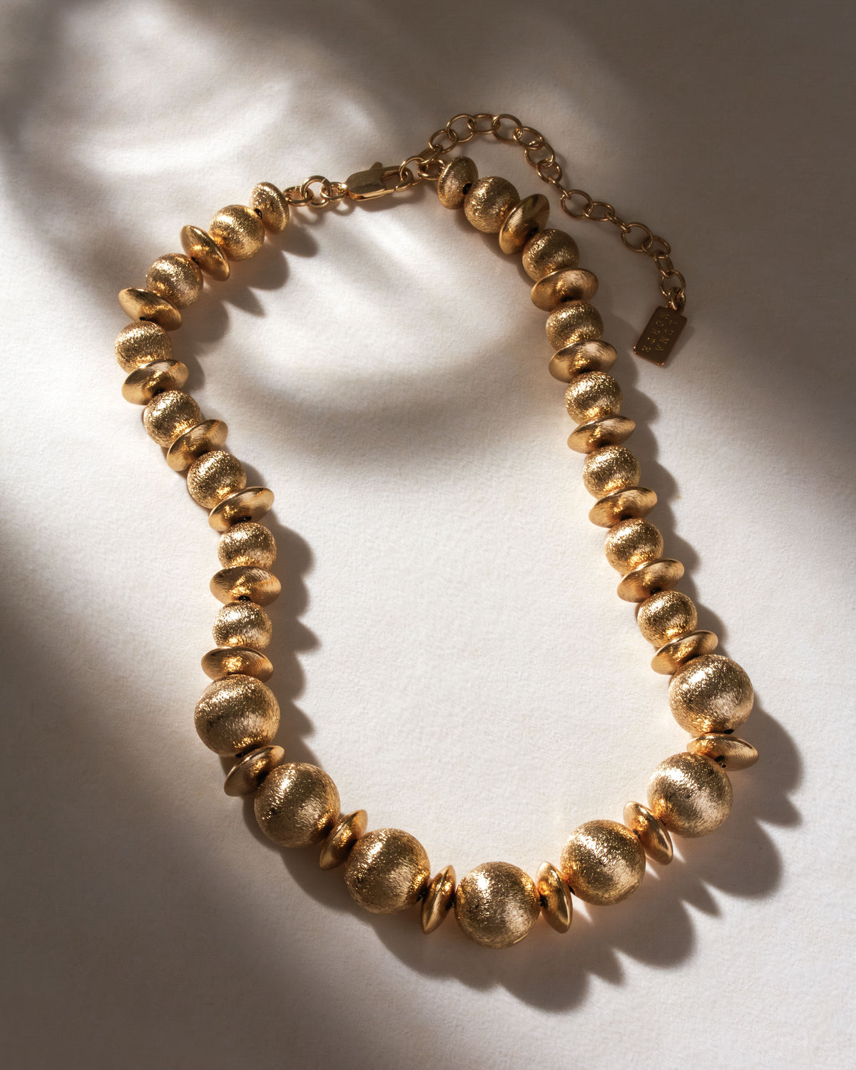 Brushed gold textured necklace with round and disc-shaped beads, and an adjustable extender chain.